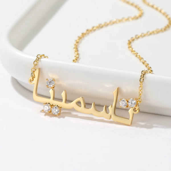 Collier personnalisé doré avec prénom arabe et pierres, sur coupelle blanche
